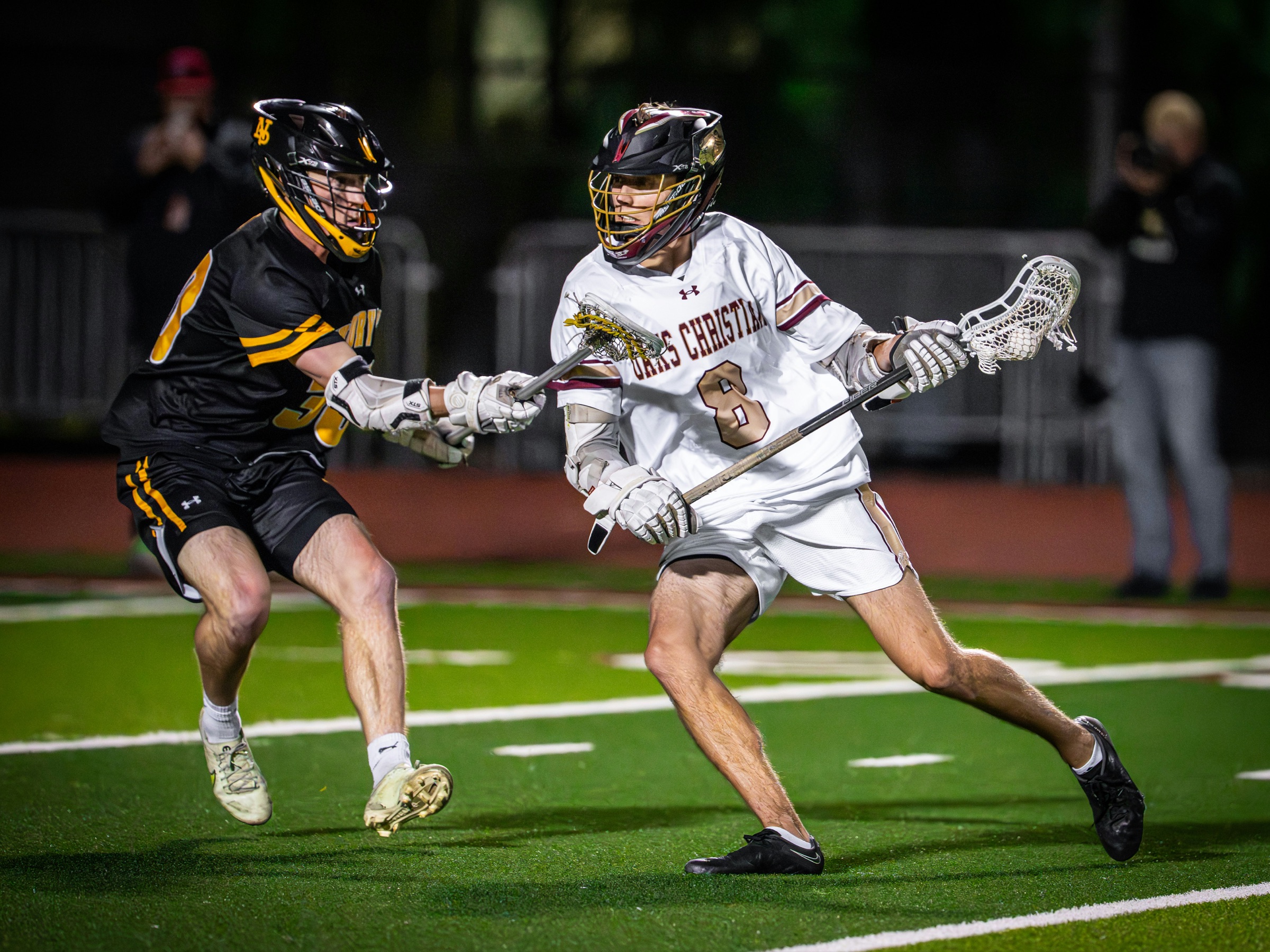 Two boys lacrosse players competing for possession during a night game